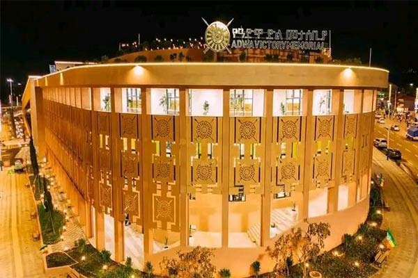 A grand, circular building lit at night, adorned with geometric patterns and a prominent Adwa Victory Memorial sign.