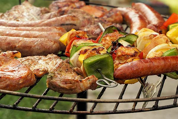  A variety of grilled meats and vegetable skewers on an outdoor grill. Sausages and sizzling kebabs create a vibrant scene. 
