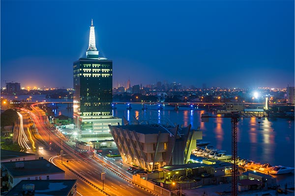 Nighttime cityscape of Lagos, Nigeria, featuring a lit modern tower and a geometric building by the water.
