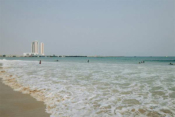 Calm Lagos beach scene with gentle waves lapping at the sandy shore. People swim and relax in the ocean.