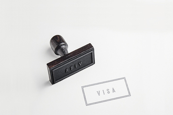Rubber stamp showing the word VISA lies diagonally on a white surface, next to its clear imprint.