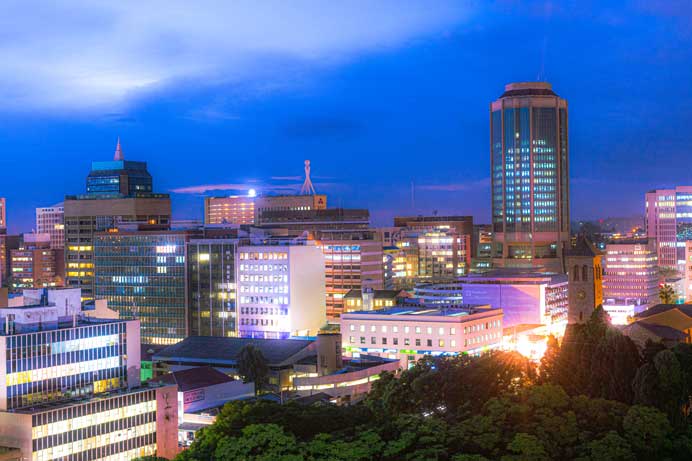  Harare city skyline at night featuring the Reserve Bank of Zimbabwe tower and illuminated office buildings.